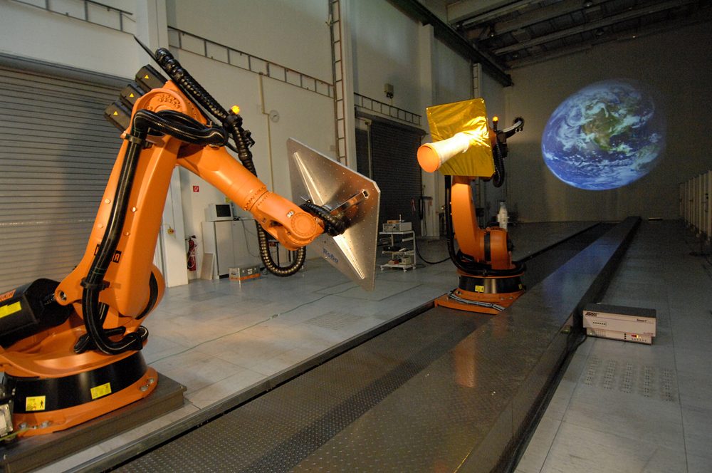 Two orange six-axis robot arms in a bright hall beside a long steel track