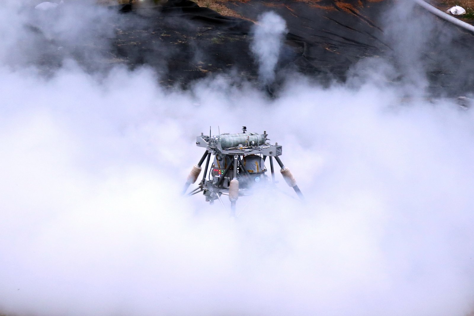 Three-legged lander hovering inside a cloud of white vapour over a test pad